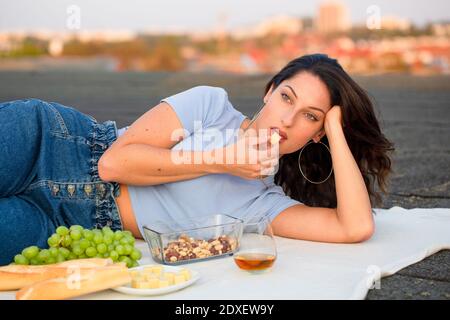 Schöne Frau, die Käse isst und auf dem Dach beim Picknick liegt Stockfoto
