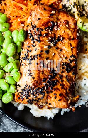 Schüssel Teriyaki Lachs mit Reis, Karottensalat, Edamame-Bohnen, Avocado und Sesam Stockfoto