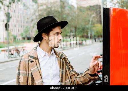 Stilvoller junger Mann mit Karomuster und Hut, Fahrrad zu mieten In der Stadt Stockfoto