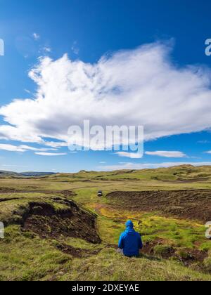 Wolken über männlichen Wanderer sitzen auf Gras und bewundern entfernt Isländische Landschaft Stockfoto