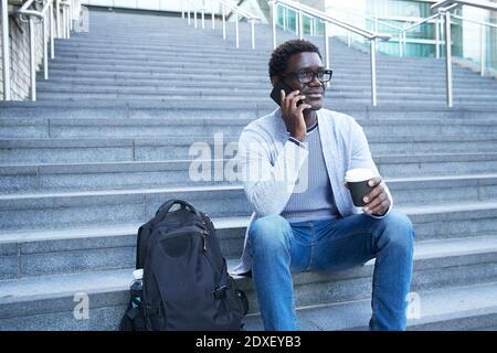 Geschäftsmann nimmt Telefonanruf ab, während er die Einweg-Kaffeetasse anhält Treppe Stockfoto
