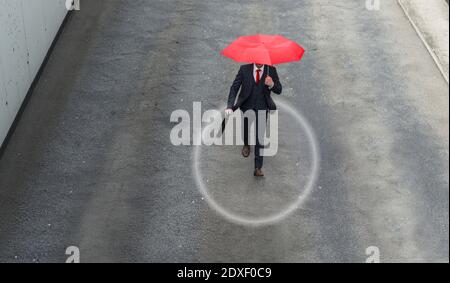 Geschäftsmann, der mit rotem Regenschirm in der Hand die Straße entlang läuft Stockfoto