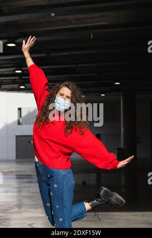 Fröhliche junge Frau trägt schützende Gesichtsmaske, während genießen sonnig Tag Stockfoto