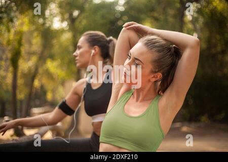 Junge Sportlerin Stretching beim Training mit Freund im Hintergrund im Freien Stockfoto