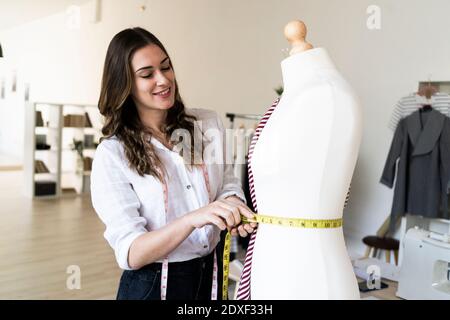Lächelnd weibliche Designerin Messung Taille von Schaufensterpuppe beim Stehen studio Stockfoto