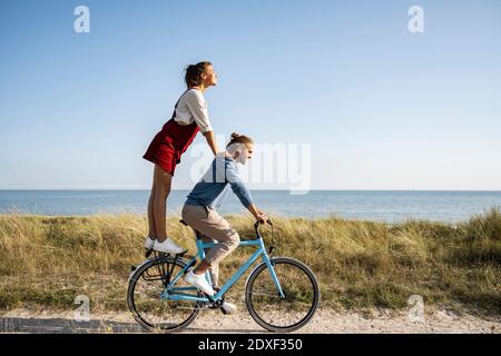 Freundin genießen Fahrt mit Mann, während auf dem Fahrrad gegen stehen Der Himmel ist klar Stockfoto