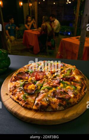 Köstliche italienische Pizza Scheibe mit Salami in der Nähe von Gemüse auf schwarz Hintergrundunschärfe im Restaurant Stockfoto