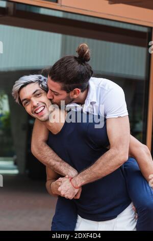 Lächelnd Mann huckbacking Gay Partner in Stadt