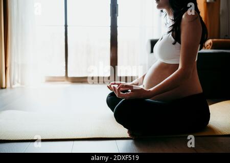 Schwangere Frau meditiert, während sie zu Hause auf der Übungsmatte sitzt Stockfoto