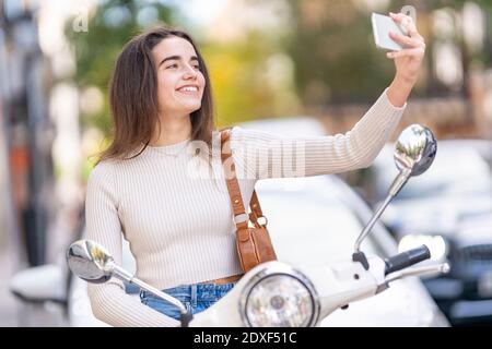 Frau mit Motorroller unter Selfie auf Smartphone Stockfoto