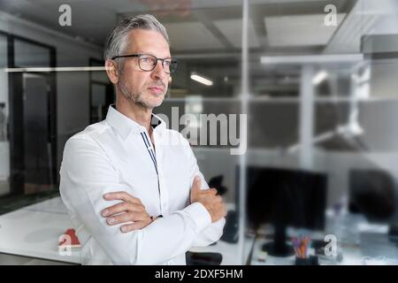 Selbstbewusster männlicher Profi mit gekreuzten Armen, die im Büro wegschauen Stockfoto