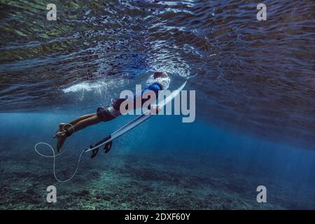 Männlicher Surfer mit Surfbrett während des Tauchens unter Wasser auf den Malediven Stockfoto