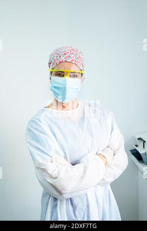 Selbstbewusster Zahnarzt trägt schützende Arbeitskleidung, die mit gekreuzten Armen steht Klinik während Covid-19 Stockfoto