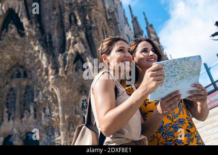 Lächelnde Freunde mit Karte, während sie gegen die Sagrada Familia in Barcelona, Katalonien, Spanien stehen Stockfoto