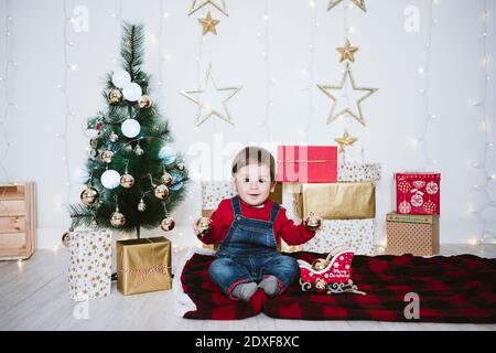 Netter Junge, der mit Kugel spielt, während er auf der Decke sitzt Zuhause während Weihnachten Stockfoto