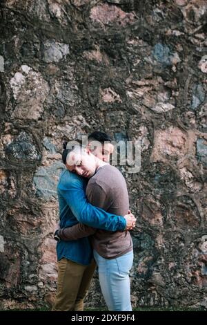Liebevolle Homosexuell Männer umarmen einander beim Stehen bei Stein Wand Stockfoto