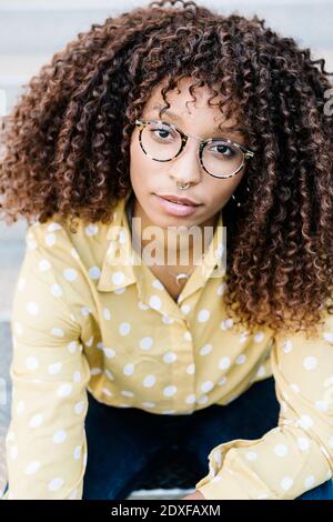 Lockiges Haar Frau trägt Brillen starren, während draußen sitzen Stockfoto