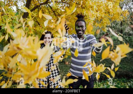 Glückliches multiethnisches Paar, das Blätter wirft, während es im Park steht Im Herbst Stockfoto