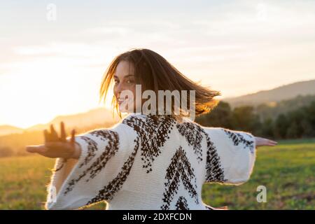 Fröhliche junge Frau, die während des Sonnenuntergangs mit ausgestreckten Armen tanzt Stockfoto