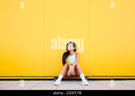 Portrait von schönen Mädchen allein auf Longboard vor gelb sitzen Wand Stockfoto