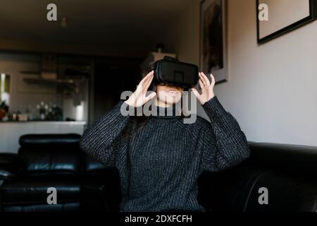 Lächelndes Teenager-Mädchen mit Virtual-Reality-Brillen, während sie auf sitzen Sofa zu Hause Stockfoto