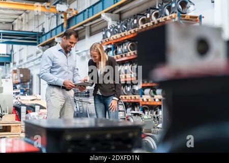 Lächelnde Geschäftsfrau und männlicher Kollege mit digitalem Tablet im Stehen In der Industrie Stockfoto