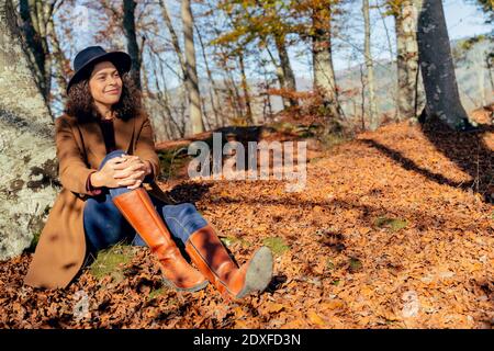 Lächelnde Frau sitzt unter Baum im Wald Stockfoto