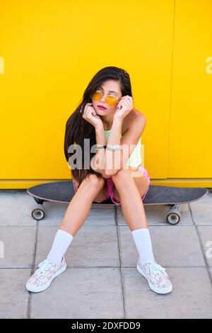 Portrait von schönen Mädchen allein auf Longboard vor gelb sitzen Wand Stockfoto