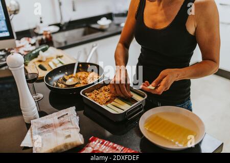 Frau legte gehackte Zucchini in Lasagne Kochplatte während des Stehens In der Küche Stockfoto