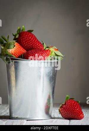 Eine Erdbeere in einem kleinen Metalleimer, der platziert wird Auf einem weißen Holzbrett.Platz kopieren Stockfoto