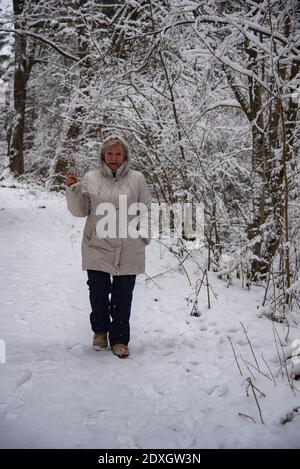 Eine ältere Frau mit grauen Haaren auf einem Spaziergang im Winterschneehalde. Stockfoto