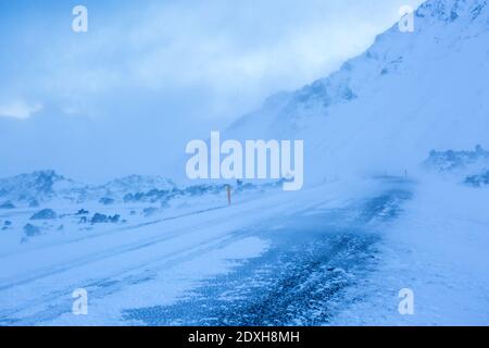 Eine Straße bei einem Schneesturm durch das Lavafeld, Snaefellsnes Peninsula, Island. Eiskruste Straße im Vordergrund. Stockfoto