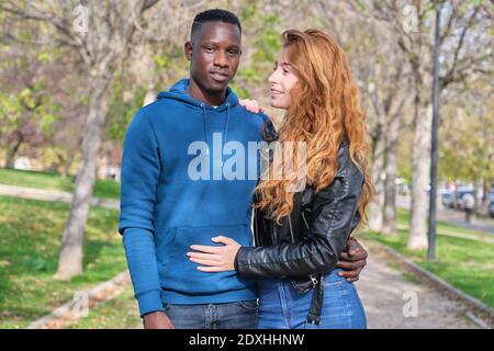 Afrikanischer schwarzer Mann und rothaarige kaukasische Frau lächeln in einem Park. Junge multirassische Paar Porträt. Stockfoto