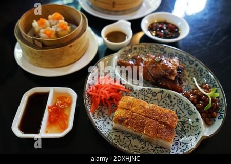 Nahaufnahme knuspriges Grillfleisch serviert mit gebratener Honigente Und Korb mit Dim Sum (chinesische Knödel) Stockfoto