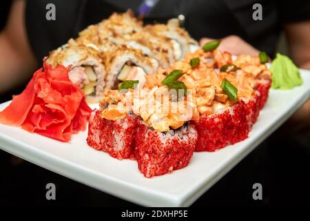 Kellner hält eine große Menge Sushi-Rollen auf einem weißen Teller. Nahaufnahme, selektiver Fokus Stockfoto