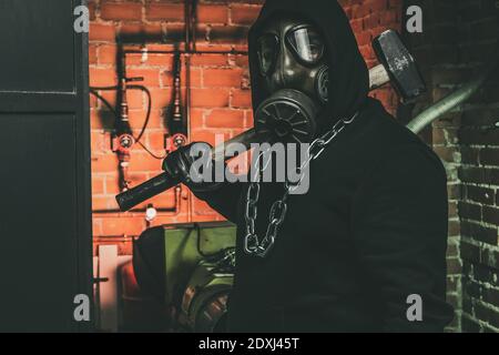 Mann mit Gasmaske und Hammer im Maschinenraum. Nukleare, biologische und chemische Gefahrenkonzept. Stockfoto