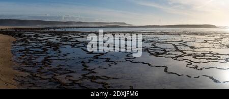 Ein Panoramablick auf goldenes Abendlicht, das sich in Gezeiten reflektiert Pools an einem felsigen Strand mit dem Meer dahinter Stockfoto