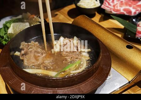 Holztisch mit Gemüse, geschnittenem Wagyu-Rind und Schweinefleisch, rohem Ei und Dipping-Sauce - Sukiyaki (japanischer Hot Pot) Stockfoto