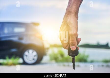 Hand halten Schlüssel und Auto auf Straßenhintergrund geparkt Stockfoto