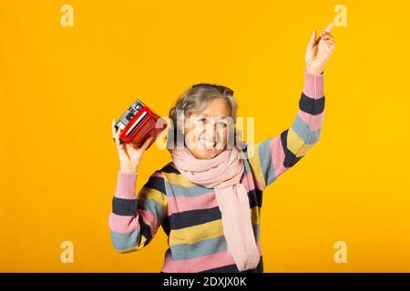 Ältere Frau in legerer Kleidung, die ein Foto mit einem sofortige Kamera vor gelbem Hintergrund Stockfoto