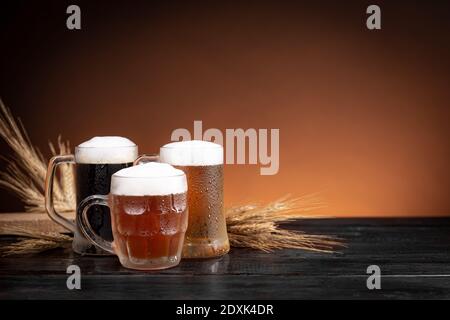 Drei Arten von kaltem Bier in Krügen und Weizenspikes auf Holzbasis. Stockfoto