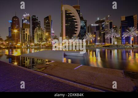 Doha Skyline in West Bay Area Doha, Katar Nachtaufnahme vom Sheraton Park mit künstlichem See im Vordergrund und Reflexion von Wolkenkratzern Stockfoto