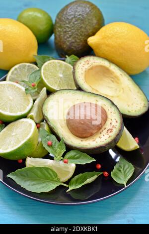 Seitenansicht einer schwarzen Platte voller gesunder Lebensmittel. Avocado, geschnittene Limetten, Zitronen und Minze auf blauem Hintergrund. Stockfoto