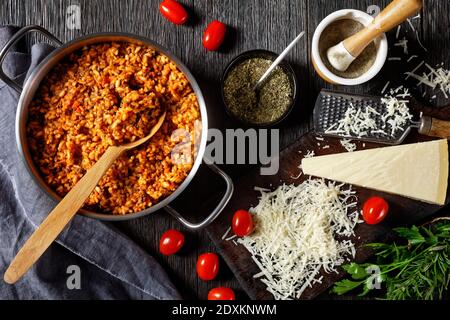 Hackfleisch Risotto in einem Metall Stevpot mit einem Löffel auf einem dunklen Holztisch mit Zutaten, italienische Küche, horizontale Ansicht von oben, flach legen Stockfoto