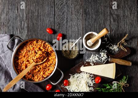 Hackfleisch-Risotto in einem Stevpot aus Metall mit einem Löffel auf einem dunklen Holztisch mit Zutaten, italienische Küche, horizontale Ansicht von oben, flaches Lay, Fr. Stockfoto