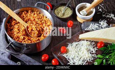 Hackfleisch Risotto Bolognese in einem Metall Stevpot mit einem Löffel auf einem dunklen Holztisch mit Zutaten, italienische Küche, Nahaufnahme Stockfoto