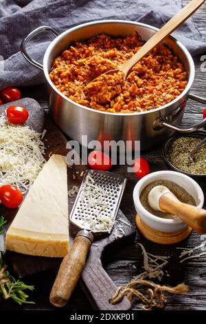 Hackfleisch Risotto in einem Metall Stevpot mit einem Löffel auf einem dunklen Holztisch mit Zutaten, italienische Küche, vertikale Ansicht von oben Stockfoto