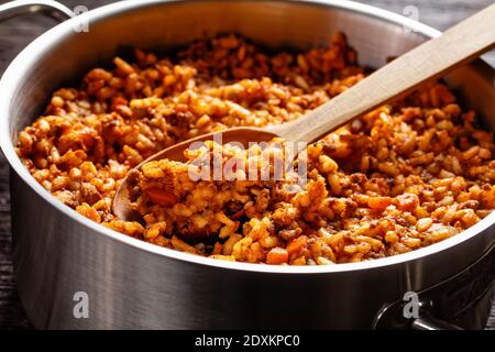 Nahaufnahme von Hackfleisch Risotto Bolognese in einem Metall Stevpot mit einem Löffel auf einem dunklen Holztisch, italienische Küche Stockfoto