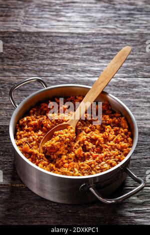 Hackfleisch Risotto Bolognese in einem Metall Stevpot mit einem Löffel auf einem dunklen Holztisch, italienische Küche, vertikale Ansicht, Freiraum Stockfoto