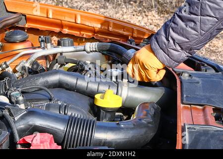 Auto-Wartung und Reparatur-Konzept. Die Hände des Fahrers in den orangefarbenen Gummihandschuhen überprüft das Auto, die offene Haube. Autos und Transport Reparatur, Nahaufnahme. Stockfoto